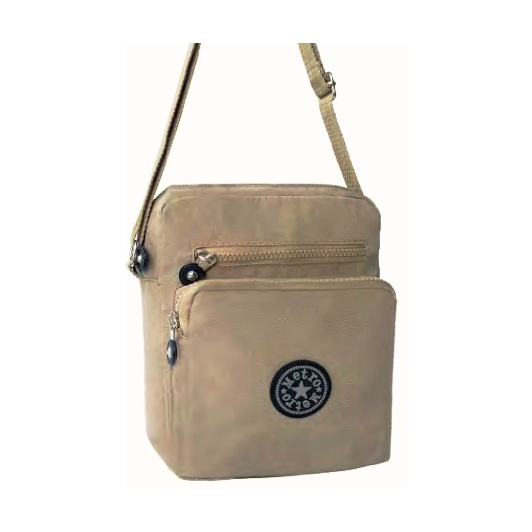 A small crossbody bag in beige, featuring a front zippered pocket with a  logo badge, a top zippered compartment, and a matching shoulder strap, shown against a plain white background.