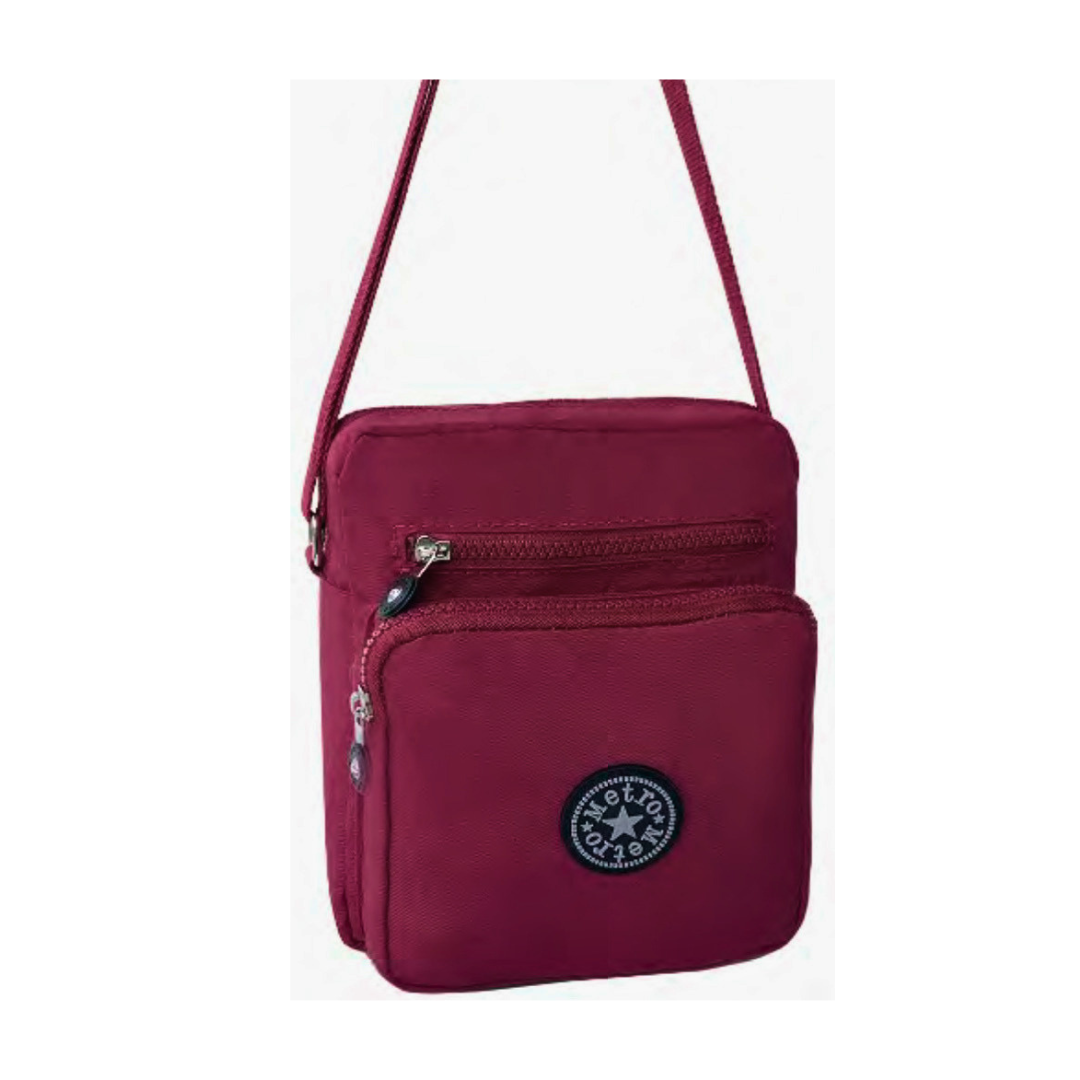 A small crossbody bag in deep burgundy, featuring a front zippered pocket with a  logo badge, a top zippered compartment, and a matching shoulder strap, shown against a plain white background.