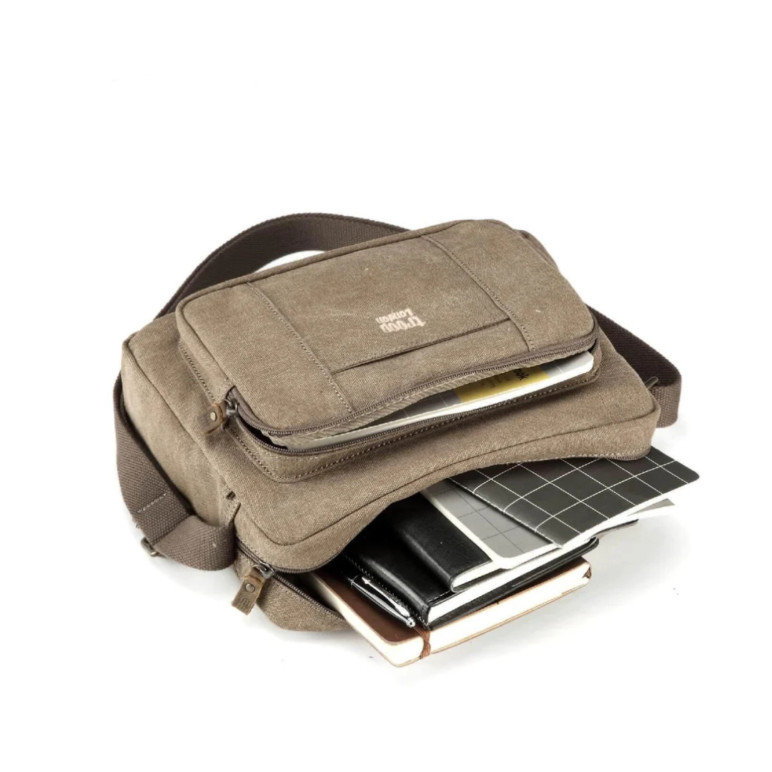 A brown Troop London Large Canvas Cross-body Bag - A4 Size & Brass Hardware with an adjustable shoulder strap, with a front zippered pocket and a shoulder strap, shown holding notebooks and a tablet on a white background.